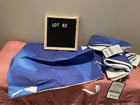Four blue and white pillow covers folded and laid on a pinkish cloth surface, with tags attached visible.