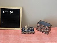 Full view of the sculpture in its decorative display case on a pink surface with a sign labeled LOT 30 in the background.
