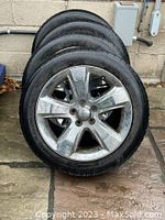 Four silver alloy wheels with mounted tires stacked outdoors against concrete wall