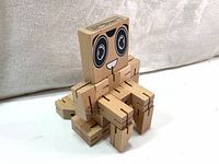 Wooden puzzle robot cube showing a sitting pose with visible face and limbs made of interlocking wooden pieces