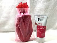 Sugar scrub tube alongside the red gift bag with tissue paper, showing the complete gift packaging included.