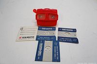 Red 3D View-Master slide viewer with four film packets and an instruction booklet laid out on a white surface.