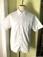 White men's short sleeve dress shirt on mannequin, showing front view with collar, button closure, and two front pockets including pen pocket