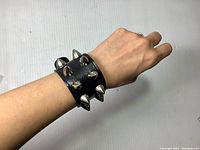 Close-up of bracelet worn on wrist showing wide black band with chrome spikes and buckle.