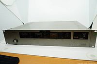 Front and top view of Panasonic AG-DA100 rack mount audio video distributor showing control panel, analog meter, output labels and rack mount ears.