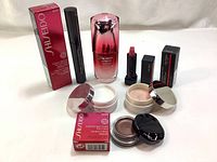 Photo shows all six products outside their packaging: two creams in jars with lids off, serum bottle, mascara tube, lipstick with cap off, and eye color in jar with lid off, alongside some product boxes.