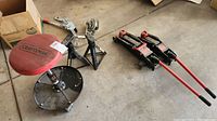 Overall view of the lot showing Craftsman rolling stool, two jack stands, and two hydraulic floor jacks on a concrete floor.