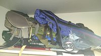 Several backpacks including black, green and blue colors stacked on shelf, some with padded back straps visible.