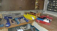 Bench with blue caulk guns, hand trowels, yellow parts organizer, and plastic boxes with small parts and soldering supplies
