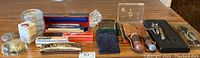 Wide view showing harmonicas, multiple hunting cutters with leather sheaths, hand warmers and other small tools and collectibles placed on a wooden surface.