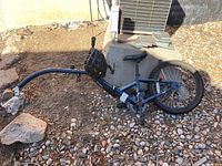 Blue Navaro Afterburner kids trailer bike lying on rocky ground showing the frame, wheel and attachment arm