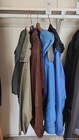 Four men's outerwear pieces on hangers showing different colors and materials, including leather jacket and various coats