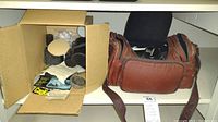 Photo of camera accessories and brown camera bag, showing assorted items packed inside and beside the bag.