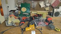 View of ten assorted corded power tools including circular saw, drills, and sanders on a workbench surface.