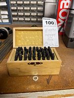 Wooden box open showing rows of metal alphabet punches standing upright in a foam-lined interior.