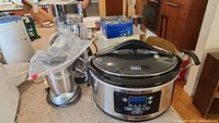 Overall view of the small kitchen appliances on a kitchen counter showing the crockpot, NutriBullet, food processor, and coffee pot.