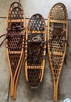 Three wooden snowshoes side by side showing frames and rawhide webbing