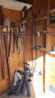 Wide view of shed corner showing hanging string trimmer and handheld blower with detachable tubes on the floor.