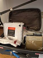 View of bedding and curtain items inside the open rolling storage case, showing labeled sheet set packaging, curtain sets, and pillow sham.