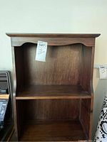 Front view of a dark wood bookcase with a scalloped edge detail on the top shelf and two shelves below.
