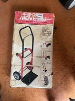 Photo of packaging box showing the 4-in-1 move handtruck and dolly with trash bag holding rack, detailing the product and its capabilities.