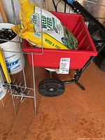 Red seed spreader with two black wheels and a bag of Expert Gardener Weed & Feed sitting inside