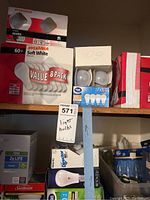 Shelf with multiple boxes of Sylvania, Philips, GE, Sunbeam light bulbs in unopened packages