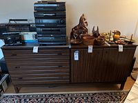 Full frontal view of the wooden MCM cabinet showing the drawer section on the left and the door cabinet on the right, with various vintage electronic equipment and decorative items on top.