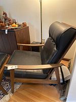 Side angle view of lounge chair with wood frame and black vinyl upholstery, footstool in front