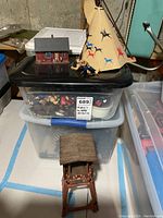 Photo showing small red house figurine and Native American teepee with painted animal designs on top of a black plastic container.