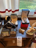 Overview of all items on table including watches in boxes, travel alarm clocks, train clock, elephant figurine clock, and small train ornament