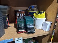 Two Boston Globe green delivery truck models along with various tins on shelf.