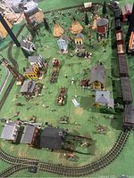 Overhead view of the western-themed train village scenery showing buildings, figures, animals, and train tracks spaced out on a green mat.