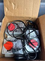 Three grey rectangular throttle/controllers stacked inside a cardboard box, each with red rotary knob and attached power cord
