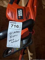 Close-up photo of the Black & Decker leaf blower with MaxSold tag showing handwritten notes: trimmer, blower, weed wacker and Black & Decker logo visible.