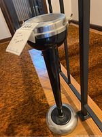 Full view of the vintage ashtray on its tall stand against a brown carpet background.