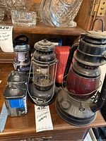 Photo showing three vintage lanterns including an Anchor brand lantern and two other metal and glass lanterns, alongside Panasonic batteries in original packaging.