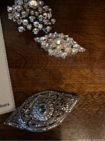 Photo of three vintage silver-tone decorative pins laid on a wooden surface showing detail and size variation