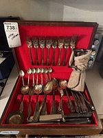 Wooden case with red felt interior holding various vintage silverplate flatware pieces, including forks, spoons, and knives, along with a fabric pouch containing additional utensils.