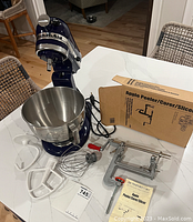 Overview of mixer, bowl, three attachments and boxed apple peeler on countertop