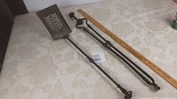 Full view of antique fireplace ash shovel with perforated metal scoop and long iron tongs beside ruler for scale.