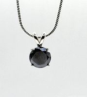 Front view of round black diamond pendant suspended on sterling silver snake chain against white background