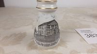 Front view showing black detailed illustration of Hay Bay U.E.L. Church and Emanuel Methodist Church with inscriptions on white ceramic vase with gold rim.