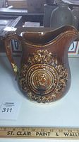 View of the full pitcher showing embossed medallion and floral scrollwork with brown glaze and lighter brown highlights.