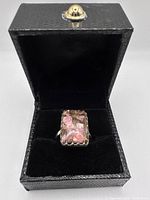 Ring with rectangular rhodochrosite stone containing natural copper veins in black textured jewelry box.