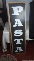 Full view of the vertical pasta sign highlighting overall size, metal front, and wooden frame.