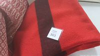Red wool blanket folded showing the black stripe and a lot number card on top.