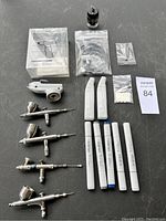 All items in the lot including airbrushes, air compressor grip, markers, and accessories arranged on a table