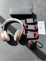 Photo showing the Beats over-ear headphones, three charging cables in black and red, Beats wireless earbud charging case with carabiner, and black box.