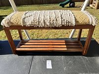 Full view of wooden bench with textured fabric cushion on top outdoors on black surface.